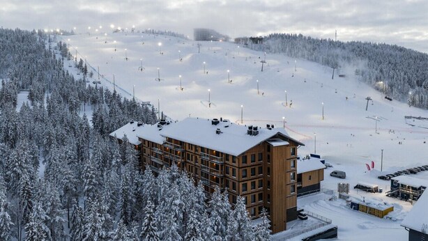 Een skigebied bedekt met sneeuw, met een houten lodge, skiliften en een besneeuwde berg op de achtergrond.