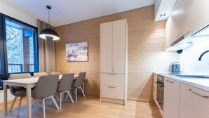 Een moderne keuken met houten kastjes, een eethoek met tafel en stoelen, en een hanglamp.