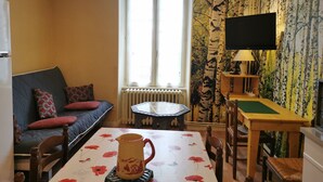Ett mysigt vardagsrum med en soffa, ett matbord med stolar, ett element, en tv och en tapet med mönster.