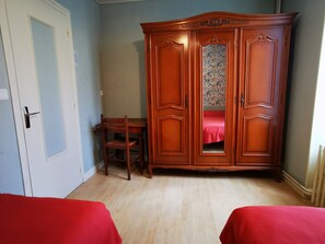 Ein Zimmer mit Holzschrank, Schreibtisch und zwei Betten mit roter Bettwäsche.