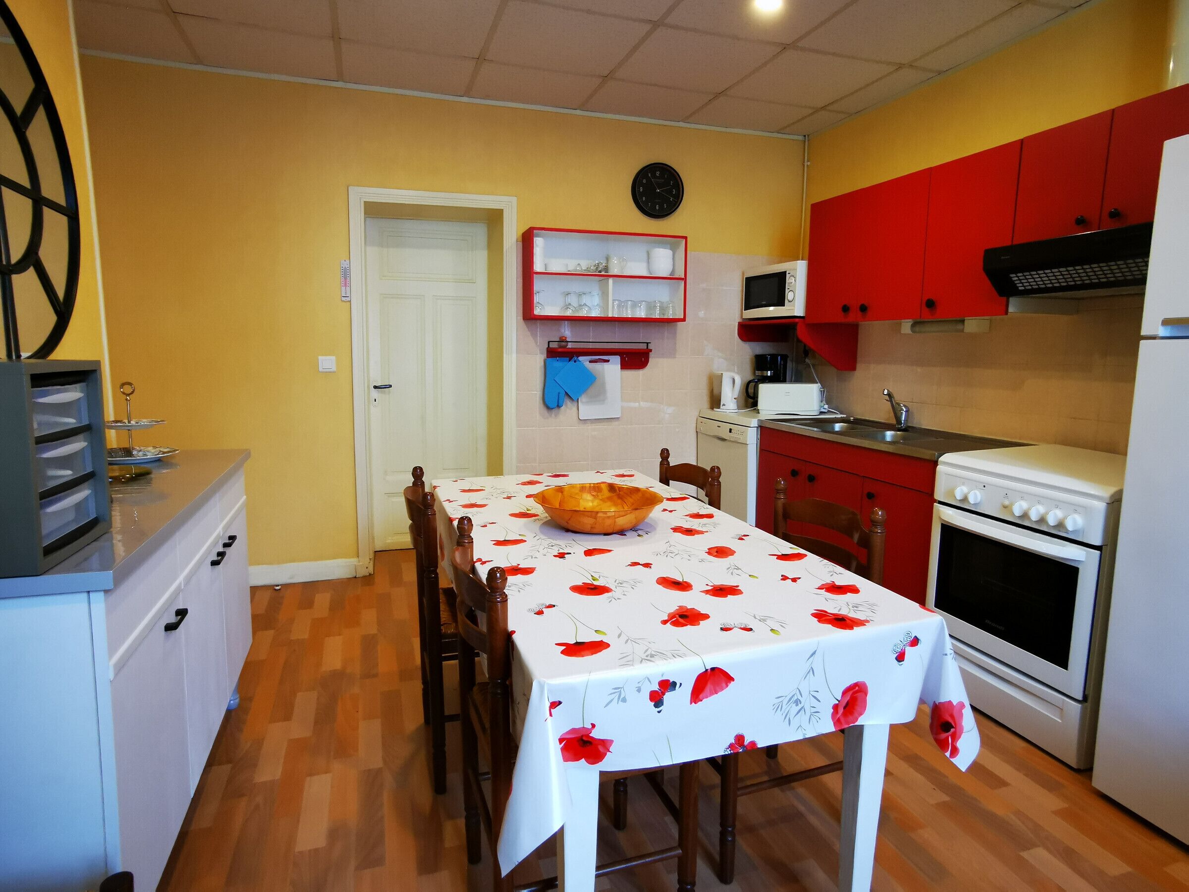 Une cuisine compacte comprenant une table à manger, des chaises en bois, un four à micro-ondes, une cuisinière et des placards rouges.