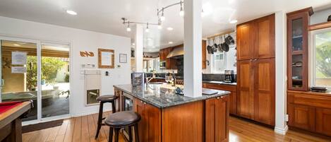 A modern kitchen with wooden cabinets, a central island with stools, and a view of the outdoor area.