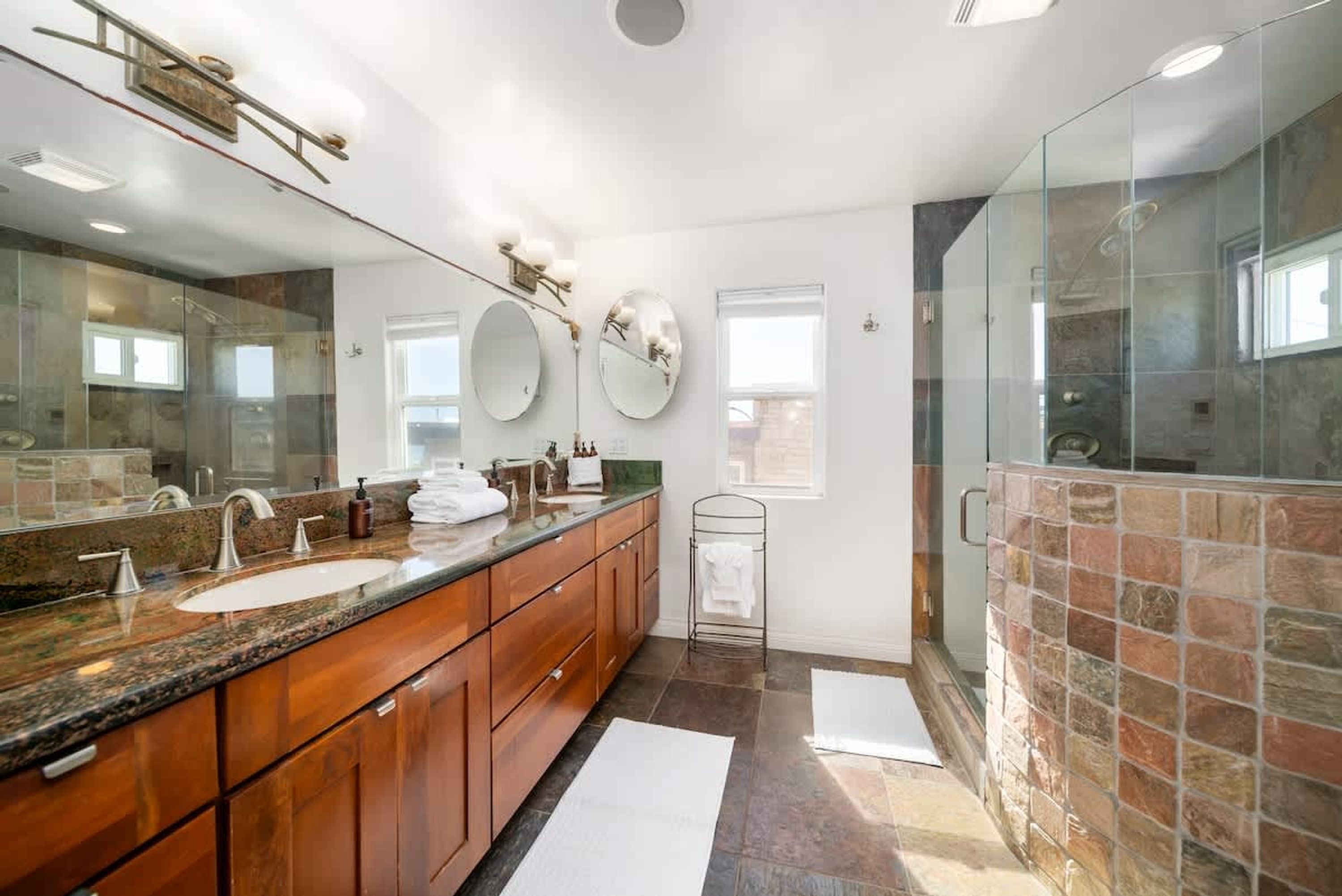 Une salle de bain moderne avec un grand miroir, un comptoir en granit, des meubles en bois et une cabine de douche en verre.
