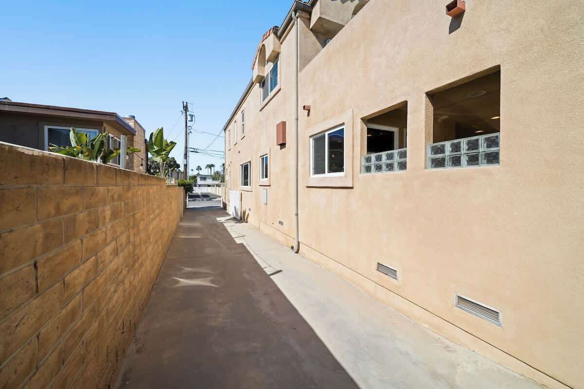 Un callejón estrecho entre edificios, con un muro de ladrillo a un lado y un edificio de color beige al otro.