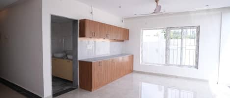 A modern kitchen with wooden cabinets and a marble countertop, a large window with bars, and a door leading to another room.