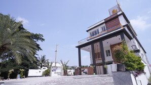 Egy modern hotel bejárata, melynek hátterében tiszta kék ég, pálmafák és egy kapuval lezárt felhajtóút látható.