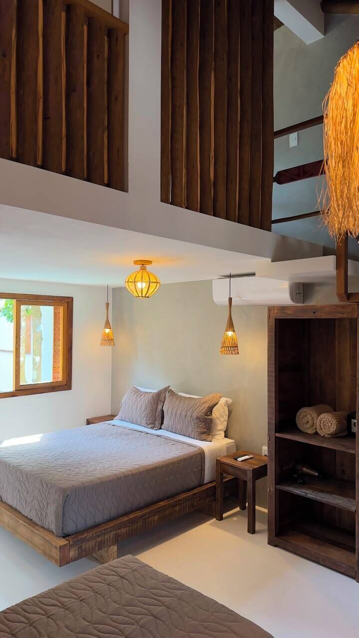 A bedroom with a large bed, wooden beams, a small table, and a hanging light fixture.