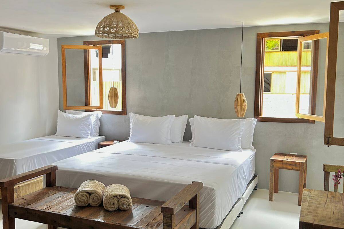 Camera da letto con un grande letto, due comodini, una panca in legno con asciugamani, una lampada a sospensione e una finestra con vista.