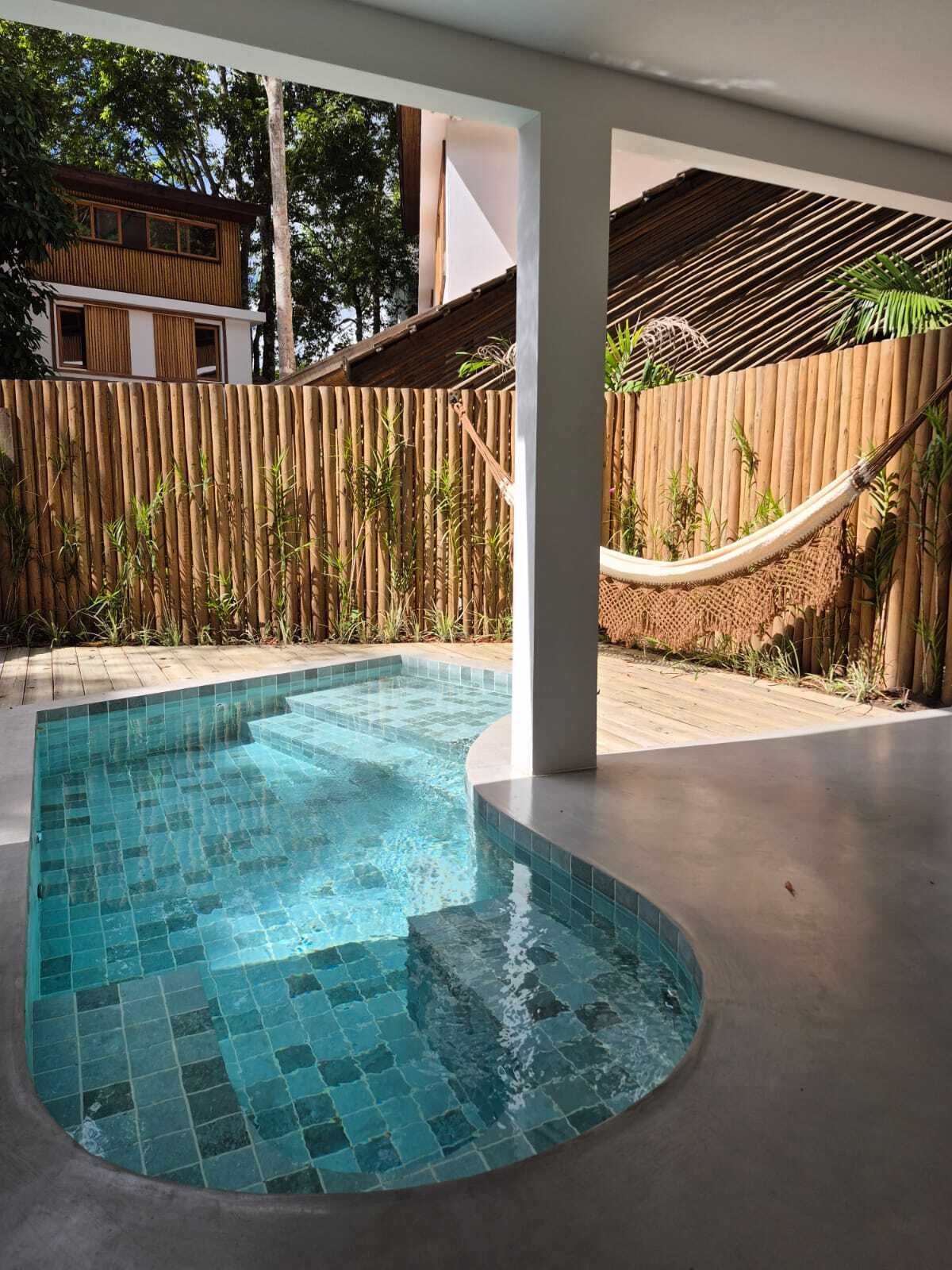 A swimming pool with a tiled edge, surrounded by a wooden fence and a hammock.