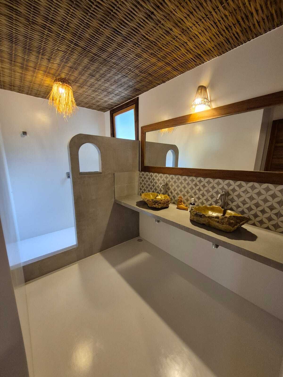 A bathroom with a modern design, featuring a large mirror, two sinks with decorative bowls, and a unique ceiling pattern.