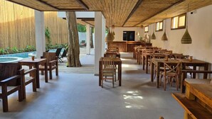Un'ampia zona pranzo all'aperto con tavoli e sedie in legno, una piscina e un'area bar.
