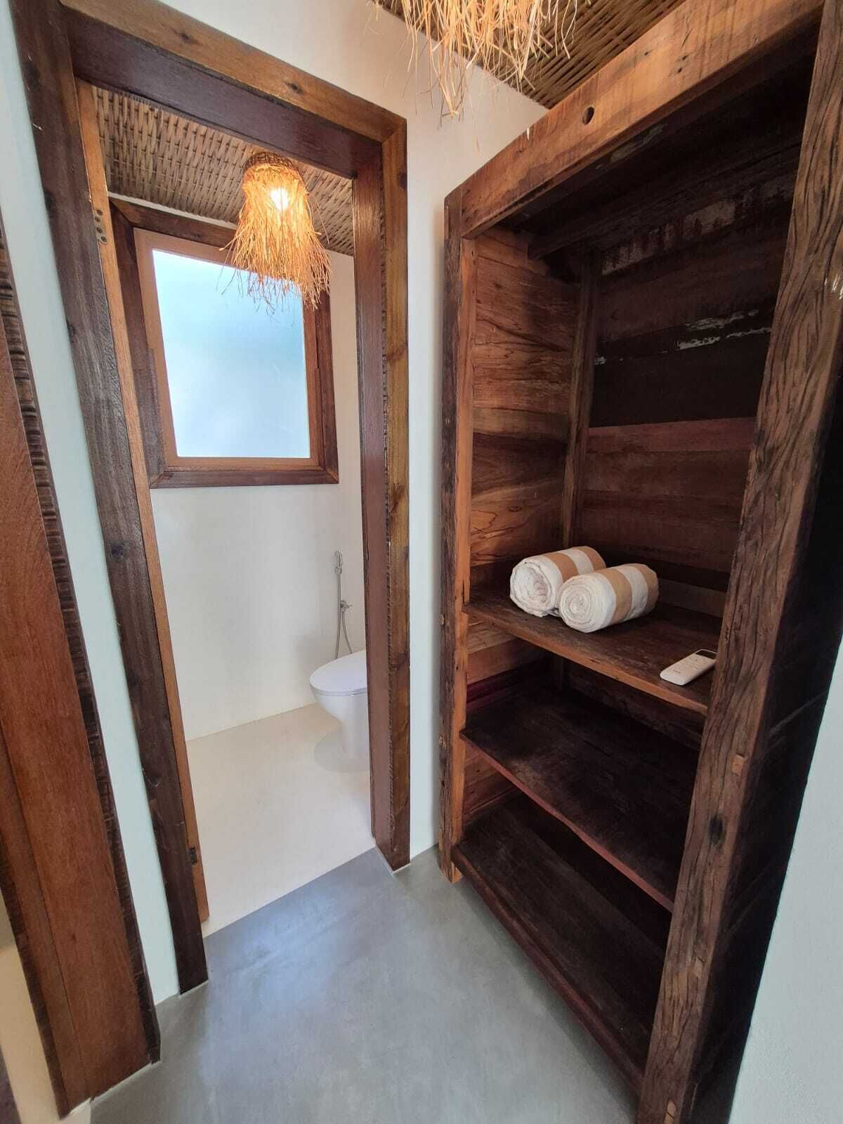 A rustic bathroom with a wooden shelf holding towels and a hanging light fixture above the sink.