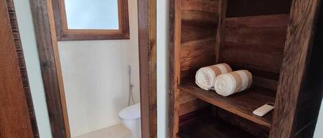 A rustic bathroom with a wooden shelf holding towels and a hanging light fixture above the sink.