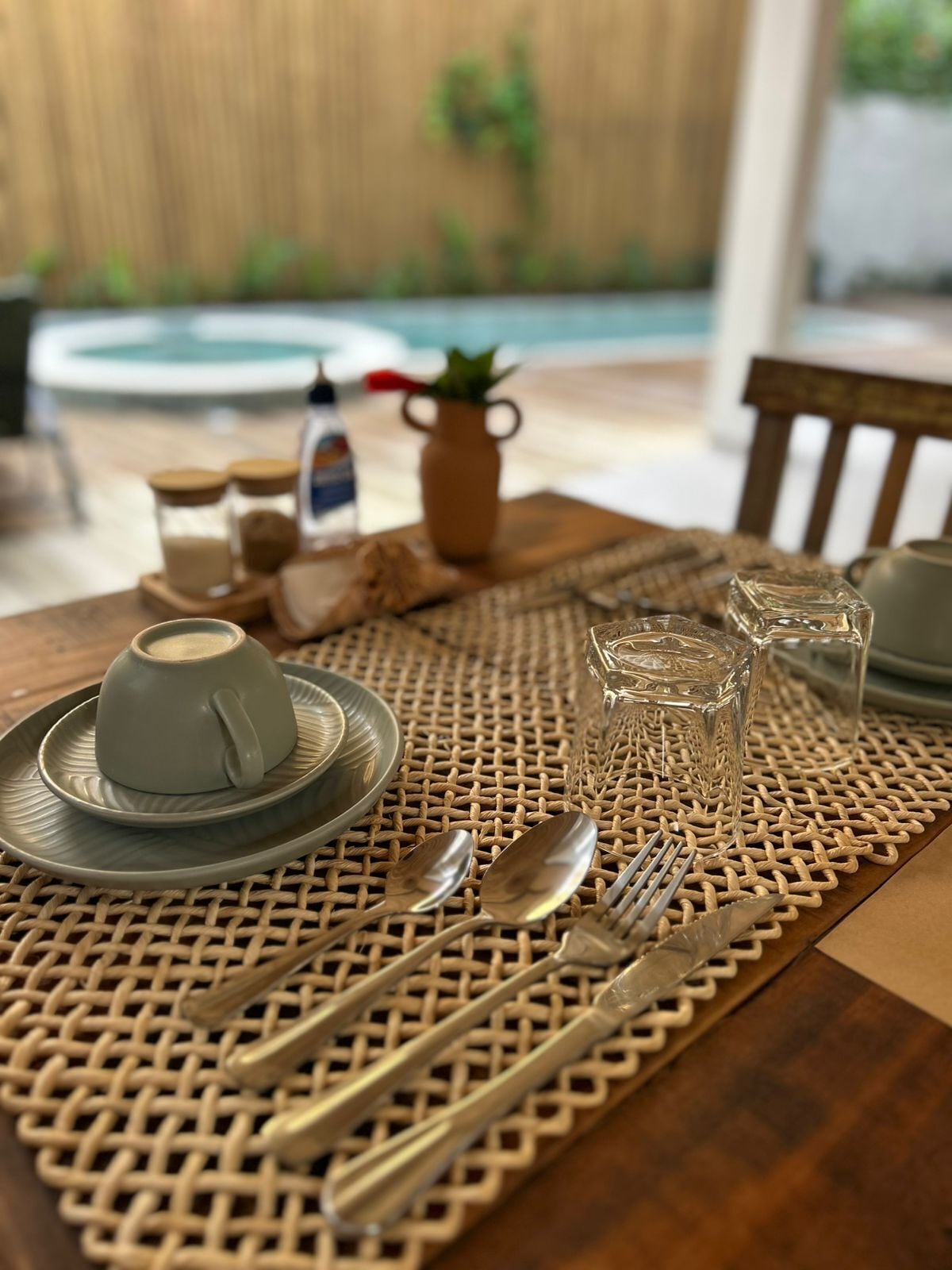 A table set with a cup, saucer, glass, cutlery, and a woven placemat.