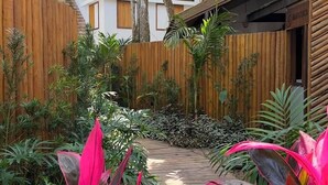 Un cortile con recinzione in legno, un vialetto e piante tropicali.