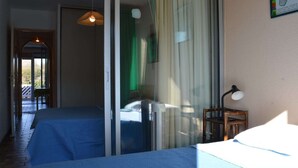 A room with two beds, a sliding glass door, a heater, a lamp, and a view of the outdoors. - 2-room Apartment - 6 people, Parking near beach (Saint-Cyprien)