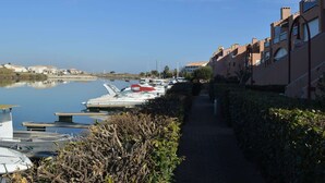 A marina with boats docked, a pathway lined with greenery, and buildings with balconies. - 2-room Apartment - 6 people, Parking near beach (Saint-Cyprien)
