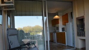 A balcony with a chair and a table, a sliding glass door leading to a kitchen with wooden cabinets and a built-in oven. - 2-room Apartment - 6 people, Parking near beach (Saint-Cyprien)