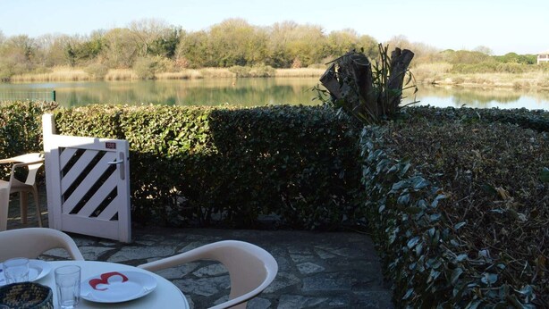 An outdoor seating area with stone flooring, a table with chairs, and a view of a lake. - 2-room Apartment - 6 people, Parking near beach (Saint-Cyprien)