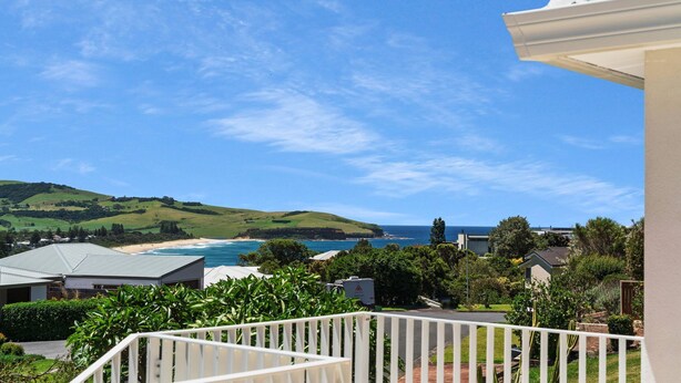 Une vue sur la côte, avec un balcon donnant sur la mer, les maisons et les collines verdoyantes.