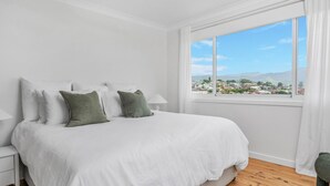 Une chambre à coucher avec un grand lit, des murs blancs et une fenêtre donnant sur une ville et des montagnes.