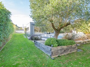 Ein Garten mit einem Baum, einem Holzpflanzkasten und einem modernen Gebäude im Hintergrund.