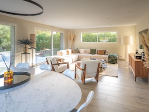 Ein modernes Wohnzimmer mit einem Ecksofa, einem Essbereich mit Marmortisch und Blick ins Grüne.