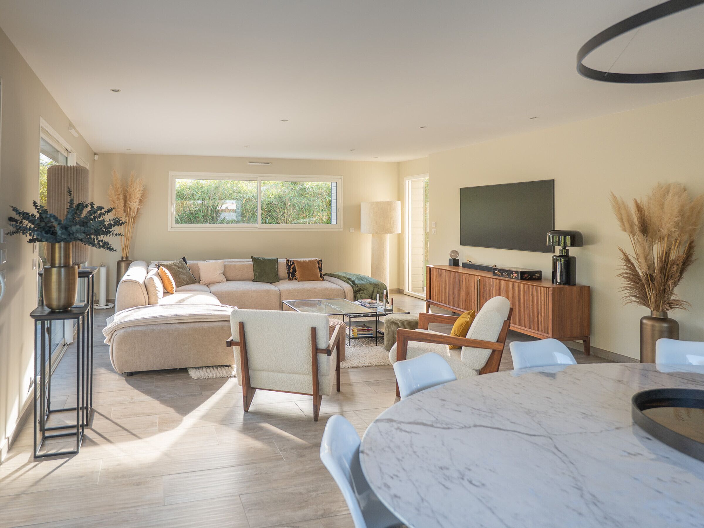 A spacious living room with a large sectional sofa, a dining table, and a TV mounted on the wall.