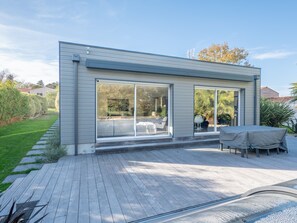 Ein modernes Haus mit großen Schiebegläsern, einer Holzdielen-Terrasse und einem überdachten Außenbereich zum Sitzen.