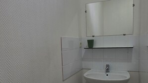 Een badkamer met een witte wastafel, een spiegel erboven en een groene beker op een plank.
