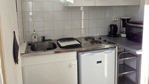Een kleine keuken met witte kastjes, een kleine koelkast, een spoelbak en een koffiezetapparaat.