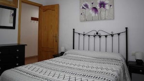 Une chambre à coucher avec un lit, une porte en bois, une table de chevet, une lampe et un tableau représentant des fleurs accroché au mur.