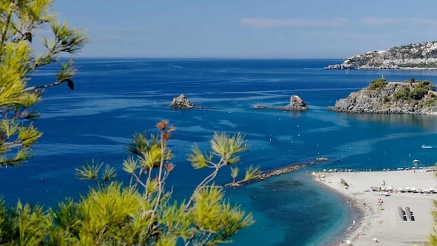 Un paysage côtier caractérisé par une eau d’un bleu limpide, des affleurements rocheux et une plage de sable.