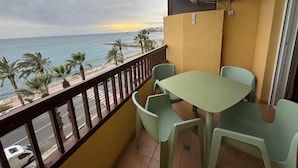 Un balcon avec une table et des chaises, donnant sur une plage bordée de palmiers et sur la mer.