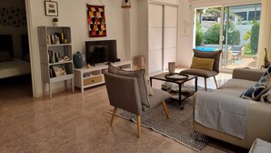 Een moderne woonkamer met een bank, fauteuil en salontafel. Er is een televisie op een dressoir, een boekenplank en een decoratief wandobject.