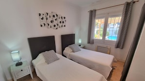 Een kamer met twee bedden, een nachtkastje met een lamp, een kunstwerk aan de muur en een raam met gordijnen.