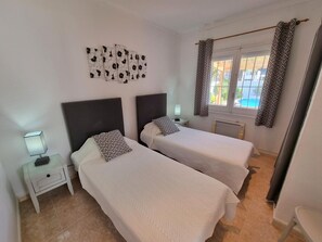 Una habitació amb dos llits, una tauleta de nit amb una làmpada, una obra d'art a la paret i una finestra amb cortines.