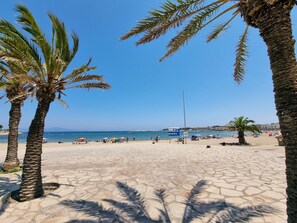 A beach with palm trees, a clear blue sky, and a signboard in the distance. - Apartment with terrace 400m from Riells beach (L'Escala)