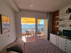 A bedroom with a bed, a TV, a desk with a chair, a balcony with a table and chairs, and a view of the marina. - Studio with Terrace Near Beach in L'Escala (L'Escala)