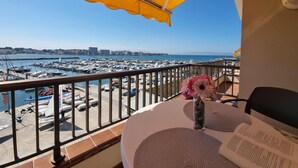 A balcony with a yellow umbrella, a table with a vase of flowers, and a view of a marina with boats. - Studio with Terrace Near Beach in L'Escala (L'Escala)