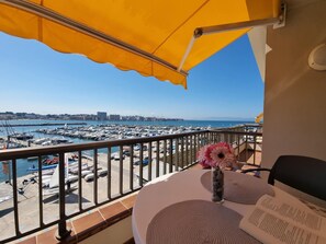 A balcony with a yellow umbrella, a table with a vase of flowers, and a view of a marina with boats. - Studio with Terrace Near Beach in L'Escala (L'Escala)