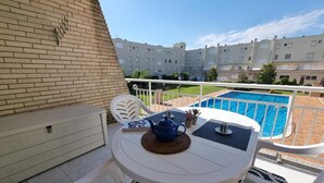 Een balkon met een tafel, stoelen en uitzicht op een zwembad en appartementencomplexen.