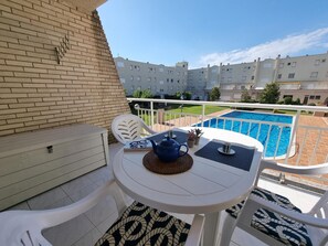 Ein Balkon mit Tisch, Stühlen und Blick auf ein Schwimmbecken sowie Wohnhäuser.