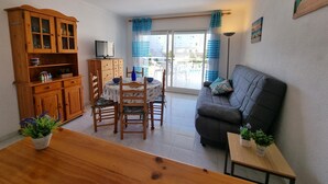 Een woonkamer met een bank, een eettafel met stoelen, een houten kast en een televisie.