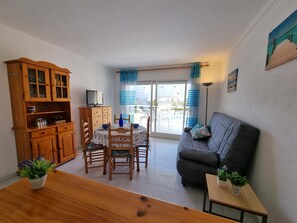 Ein Wohnzimmer mit einer Couch, einem Esstisch mit Stühlen, einem Holzschrank und einem Fernseher.