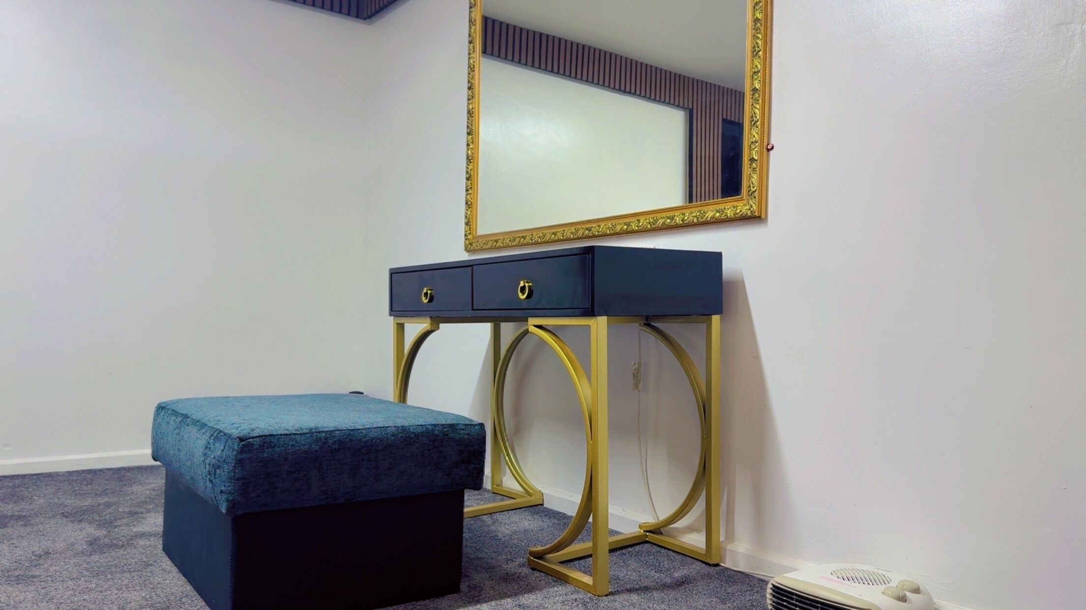A room with a dark blue vanity table with gold legs, a matching bench, and a large mirror with a gold frame.