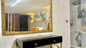 Een kamer met een grote spiegel, een zwarte console tafel met gouden poten en een groene bekleden bank.