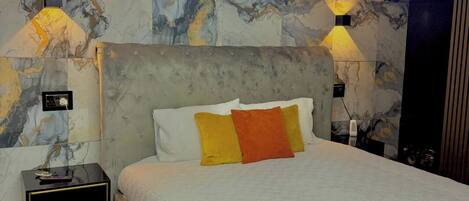Un dormitorio moderno con una pared con estampado de mármol, una cama grande con almohadas blancas y anaranjadas, y dos lámparas de pared.