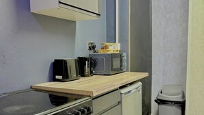 Een kleine keuken met een kookplaat, oven, magnetron en een vuilnisbak.