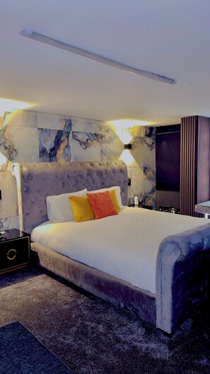 Une chambre à coucher moderne avec une tête de lit capitonnée, un grand lit, une table de chevet, un téléviseur et des murs à motifs de marbre.